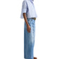 A person models the TWP Next Ex Stripe Shirt in light blue with wide-leg jeans, a brown belt, and brown shoes, standing against a white background.
