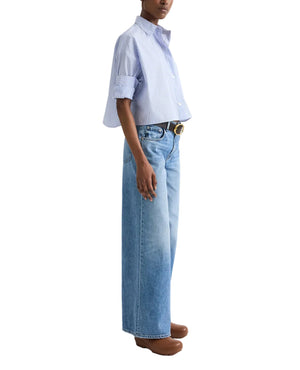 A person models the TWP Next Ex Stripe Shirt in light blue with wide-leg jeans, a brown belt, and brown shoes, standing against a white background.