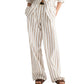 A person wears TWP's Hudson St. Cotton Stripes Pant—a white, wide-leg, brown pinstripe style—paired with a matching button-up shirt, brown sandals, and a black belt. Hands are casually tucked in pockets.