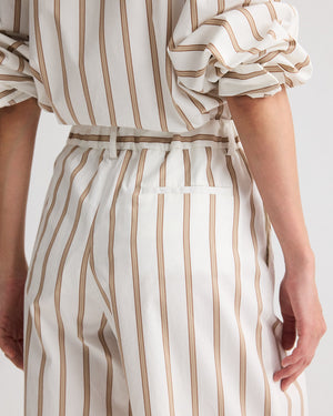 Model wearing the Hudson St. Cotton Stripes Pant by TWP, a wide-leg, mid-rise style with vertical beige stripes, paired with a matching white pinstripe shirt. Sleeves are rolled up; shown from back and side views.