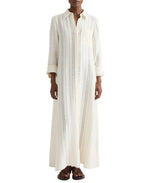 A person wearing TWP's Jenny's Ladder Weave Linen Gown, an oversized maxi shirtdress with a relaxed silhouette and vertical perforated stripes, paired with black sandals.