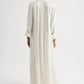 Model shown from the back wearing TWP's Jenny's Ladder Weave Linen Gown, an oversized maxi shirtdress with a relaxed silhouette and vertical ladder weave cut-out stripes, standing against a plain background.