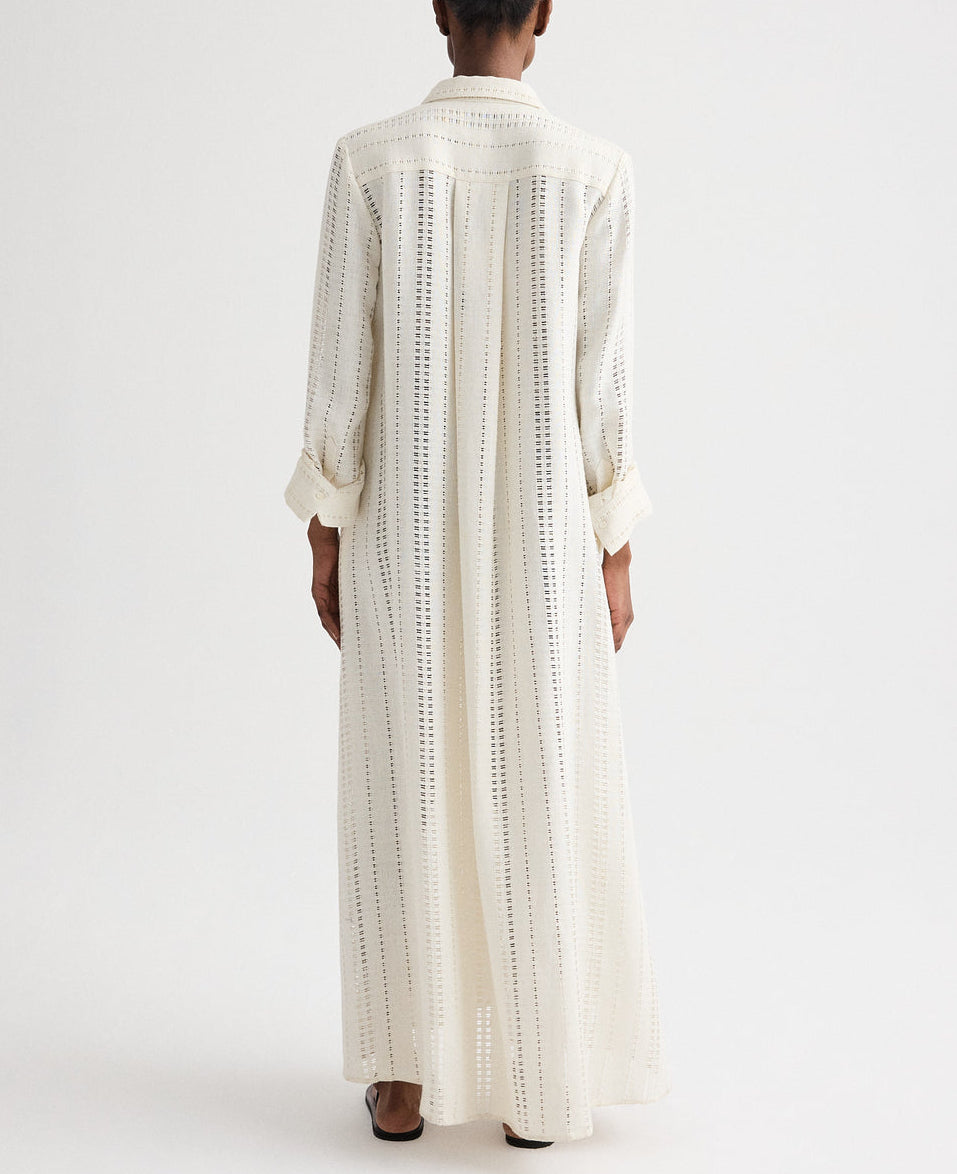 Model shown from the back wearing TWP's Jenny's Ladder Weave Linen Gown, an oversized maxi shirtdress with a relaxed silhouette and vertical ladder weave cut-out stripes, standing against a plain background.