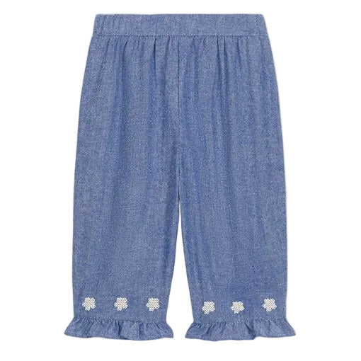 The Louise Misha Baby Girls’ Mikani Set features blue chambray pants with ruffled hems and delicate white floral embroidery near the bottom of each leg, evoking the charm of an embroidered baby outfit. Shown against a white background, this set is perfect for creating a stylish look when paired with your favorite blouse.