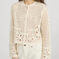 A woman wearing Frame’s The Postcard Cardi, a cream-colored, long-sleeve crochet cardigan with a round neckline, paired with cream pants.