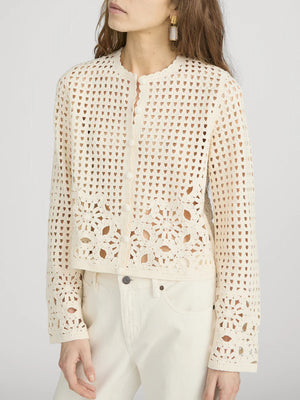 A woman wearing Frame’s The Postcard Cardi, a cream-colored, long-sleeve crochet cardigan with a round neckline, paired with cream pants.