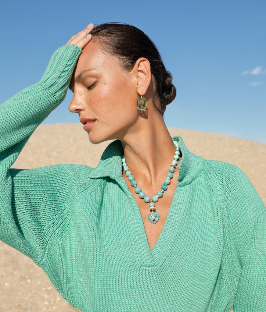 A woman in a green blouse accessorized with Lizzie Fortunato Tile Earrings, posing in a desert setting, hand touching her head.