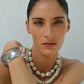 A woman with slicked-back hair wears the Laguna Necklace by Lizzie Fortunato and a chunky translucent bracelet, posing against a plain light background.