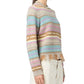 A person in the Western Stripe Crew sweater by Guest in Residence, featuring multicolored stripes and a fringe hem, paired with light-colored pants, shown from the side against a white background.