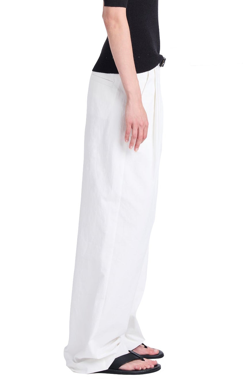 Dressed in a black top and oversized white Proenza Schouler Helena Pant, paired with black sandals, an individual poses in profile against a white background, highlighting the relaxed silhouette.