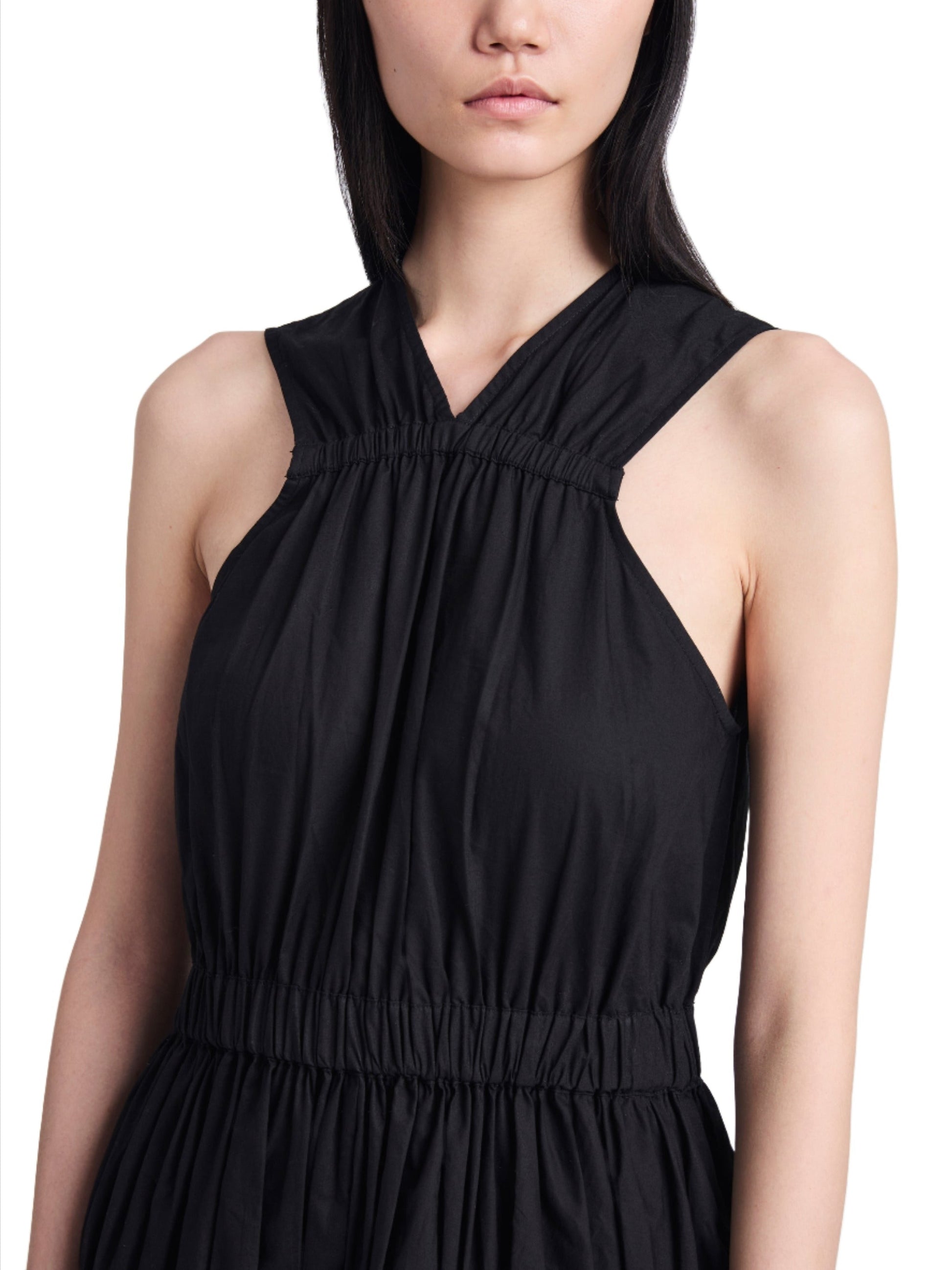 A woman models a sleeveless black Proenza Schouler Libby Dress, focusing on the ruched bodice and criss-cross neckline detail. Only her torso and face are visible against a light background.