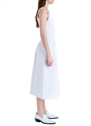 A woman with long hair wearing the Proenza Schouler Shelby Dress, a sleeveless white cotton linen piece featuring a fit and flare silhouette, stands in side profile against a white background.