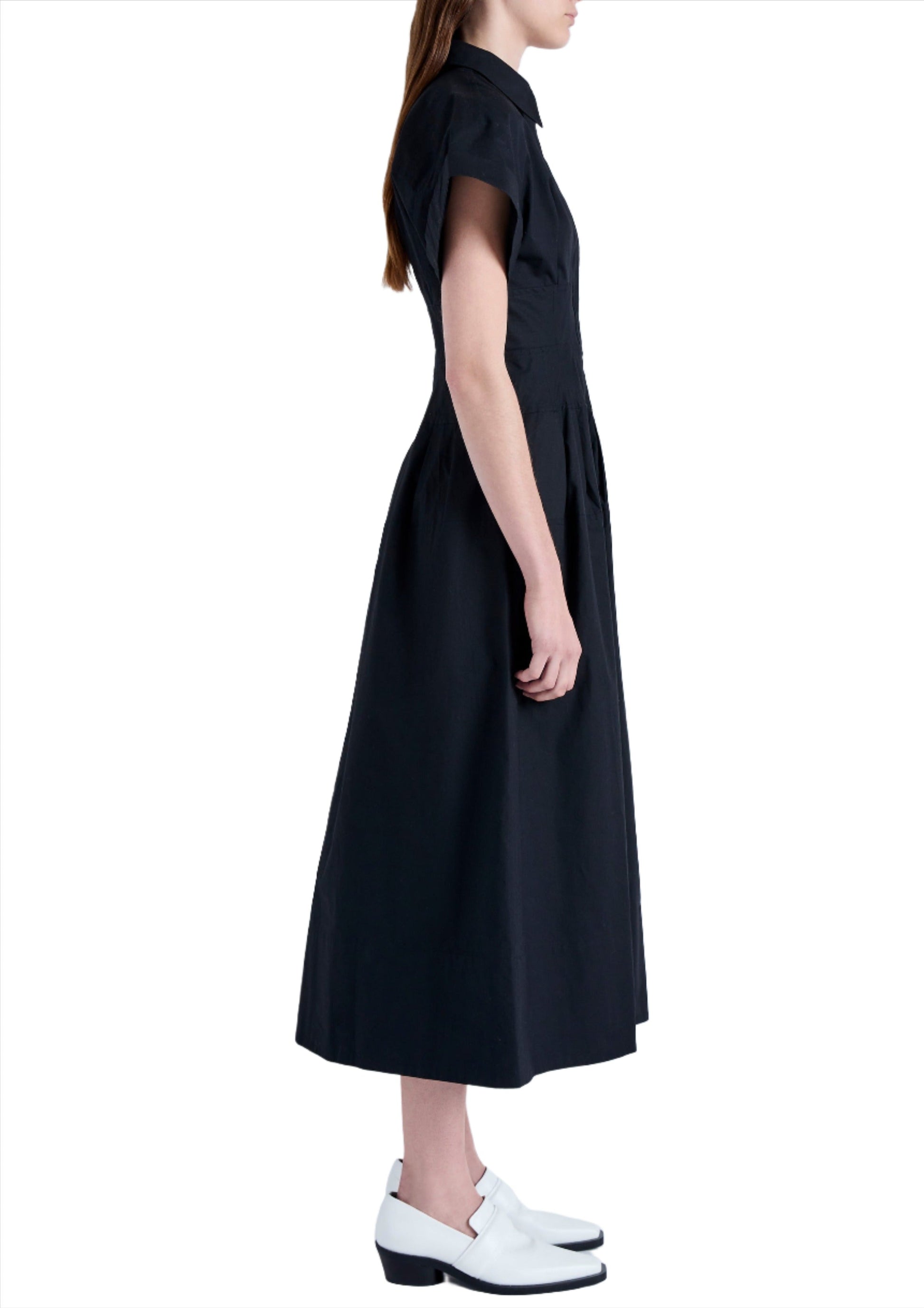 Side view of a person standing in a black, short-sleeve, knee-length Proenza Schouler Balston Dress paired with white shoes.