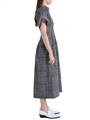 Side profile of a person wearing the Proenza Schouler Balston Grid Poplin Dress by Proenza Schouler White Label, featuring a black and white checkered A-line design with a point collar, paired with white shoes against a plain background.