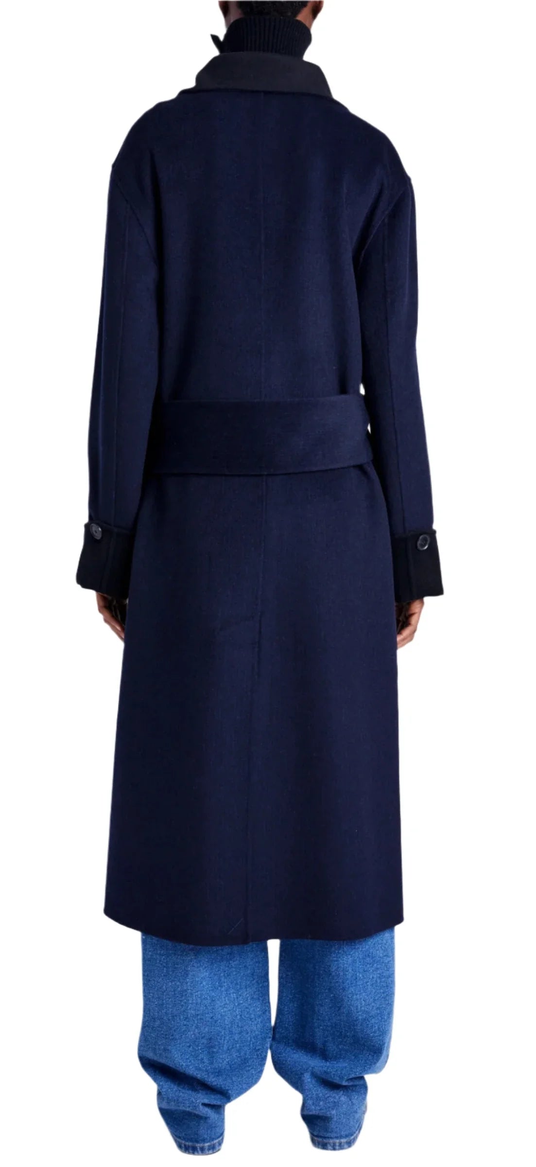 Facing away from the camera, a person wears the Proenza Schouler White Label's Constance Pinstripe Melton Coat, characterized by a dark blue hue with a self-tie belt and double-breasted silhouette, matched with light blue jeans.