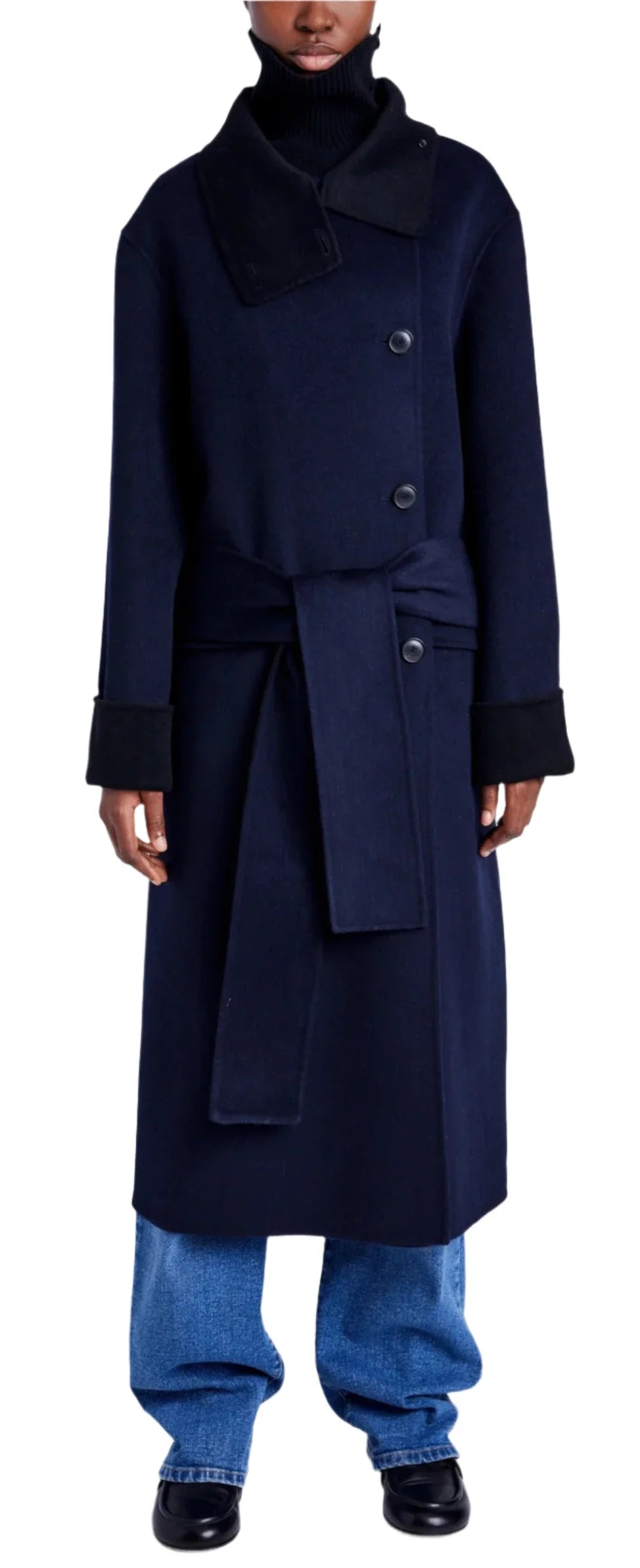 Dressed in the Proenza Schouler White Label Constance Pinstripe Melton Coat, featuring a wide collar, large buttons, a double-breasted silhouette, black cuffs, and a self-tie belt, paired with blue jeans and black shoes.