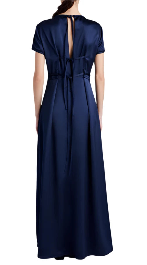 Back view of a woman in a floor-length, dark blue Proenza Schouler White Label Delphine Satin Dress featuring an A-line silhouette, tied waist, and open back detail.