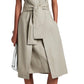 Someone is wearing the Proenza Schouler White Label Caro Dress Brushed Poplin, showcasing an A-line silhouette, sleeveless design, and self-tie waist belt. This beige dress with pockets is stylishly paired with black sandals and a sleek white clutch.