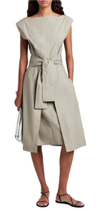 Someone is wearing the Proenza Schouler White Label Caro Dress Brushed Poplin, showcasing an A-line silhouette, sleeveless design, and self-tie waist belt. This beige dress with pockets is stylishly paired with black sandals and a sleek white clutch.
