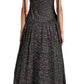A person stands with their back to the camera wearing a black Proenza Schouler White Label Clayton Dress Printed Poplin with white speckles, sleeveless and tied shoulders. The ankle-length dress pairs elegantly with flat black sandals.