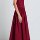 A woman in a sleeveless, ankle-length burgundy Kendall Dress by Proenza Schouler White Label, featuring a scoop neckline and crafted from soft Tech Cotton, stands in profile against a plain light background wearing black sandals.