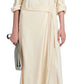 A person in a Proenza Schouler White Label Lato Wrap Dress Linen Slub in cream holds a small gray clutch and wears black sandals.