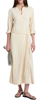 A person in a Proenza Schouler White Label Lato Wrap Dress Linen Slub in cream holds a small gray clutch and wears black sandals.