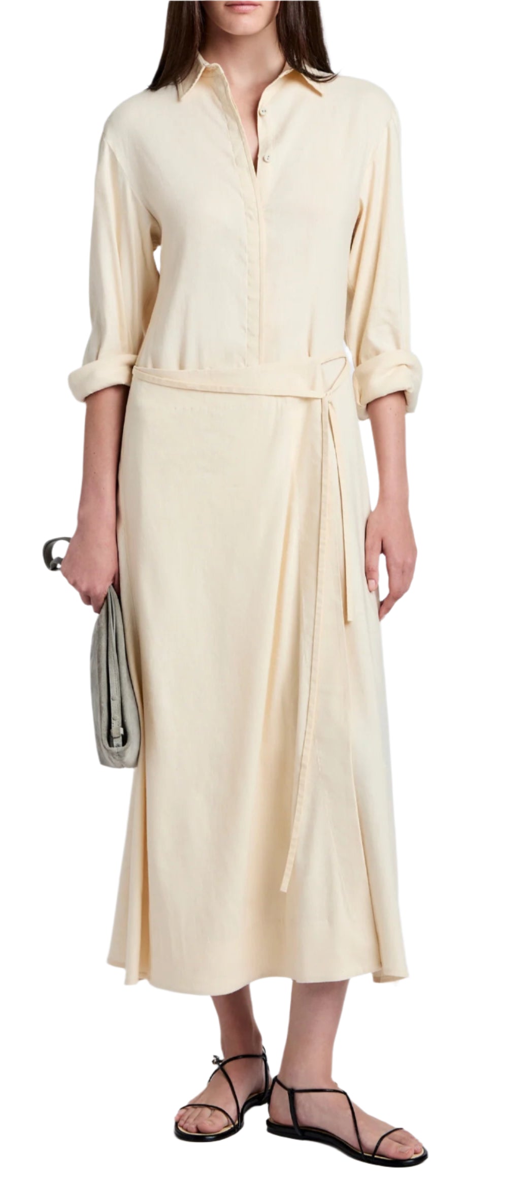 A person in a Proenza Schouler White Label Lato Wrap Dress Linen Slub in cream holds a small gray clutch and wears black sandals.