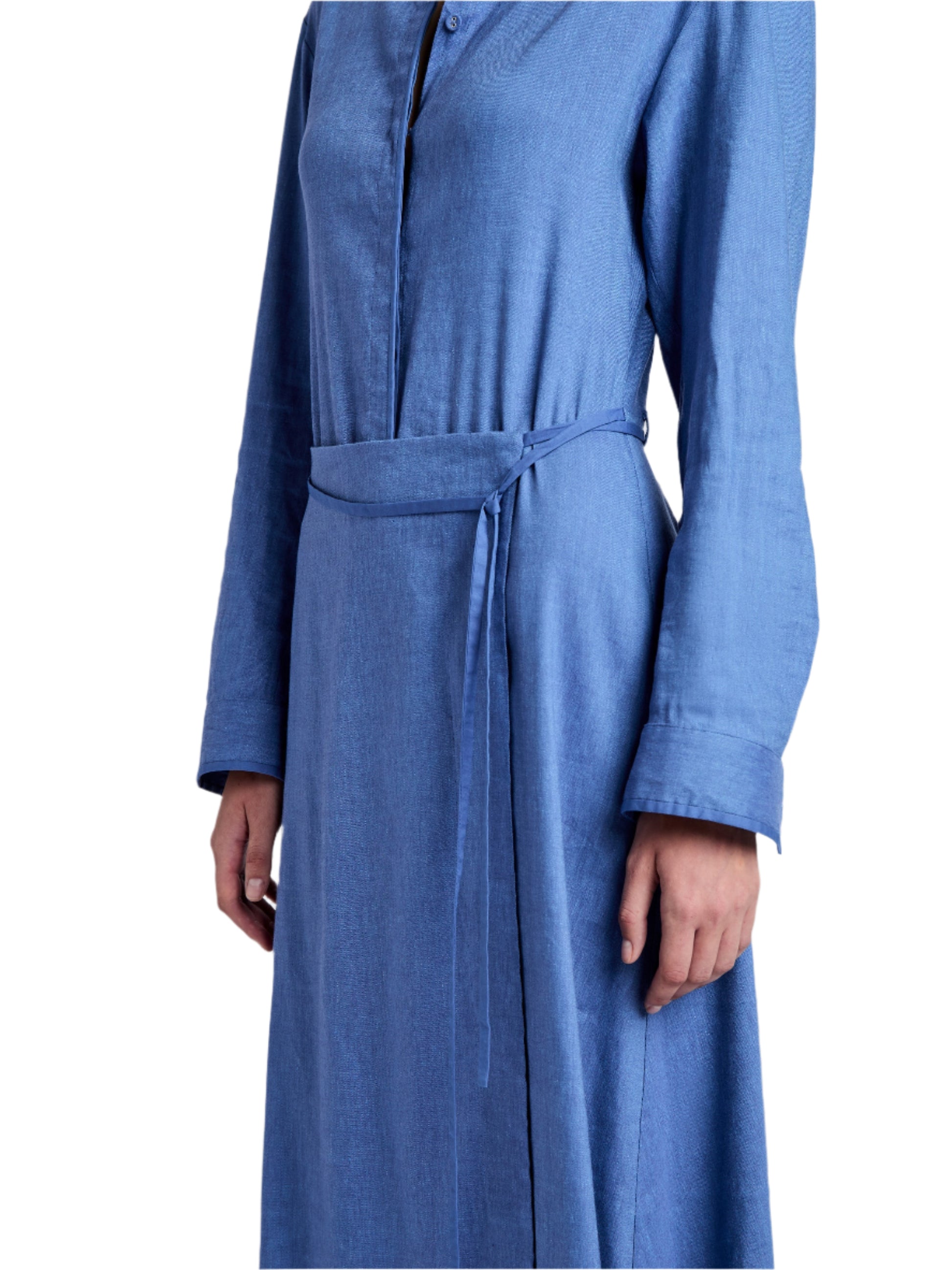 Wearing the Lato Wrap Dress Linen Slub by Proenza Schouler White Label, a person stands in a blue long-sleeve wrap dress with a shirtdress silhouette and tied belt elegantly accentuating the waist, as they face slightly to the side.