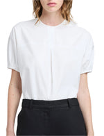 Against a plain background, the person wears the Proenza Schouler White Label Haleigh Top in cotton sateen. Its white short sleeves are tucked into black pants, effortlessly combining elegance with simplicity.