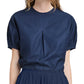 The person is wearing a Proenza Schouler White Label Haleigh Top in dark blue, featuring short sleeves and pleated front detail, paired with a matching Cotton Sateen skirt.