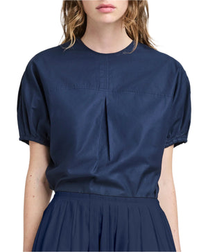The person is wearing a Proenza Schouler White Label Haleigh Top in dark blue, featuring short sleeves and pleated front detail, paired with a matching Cotton Sateen skirt.