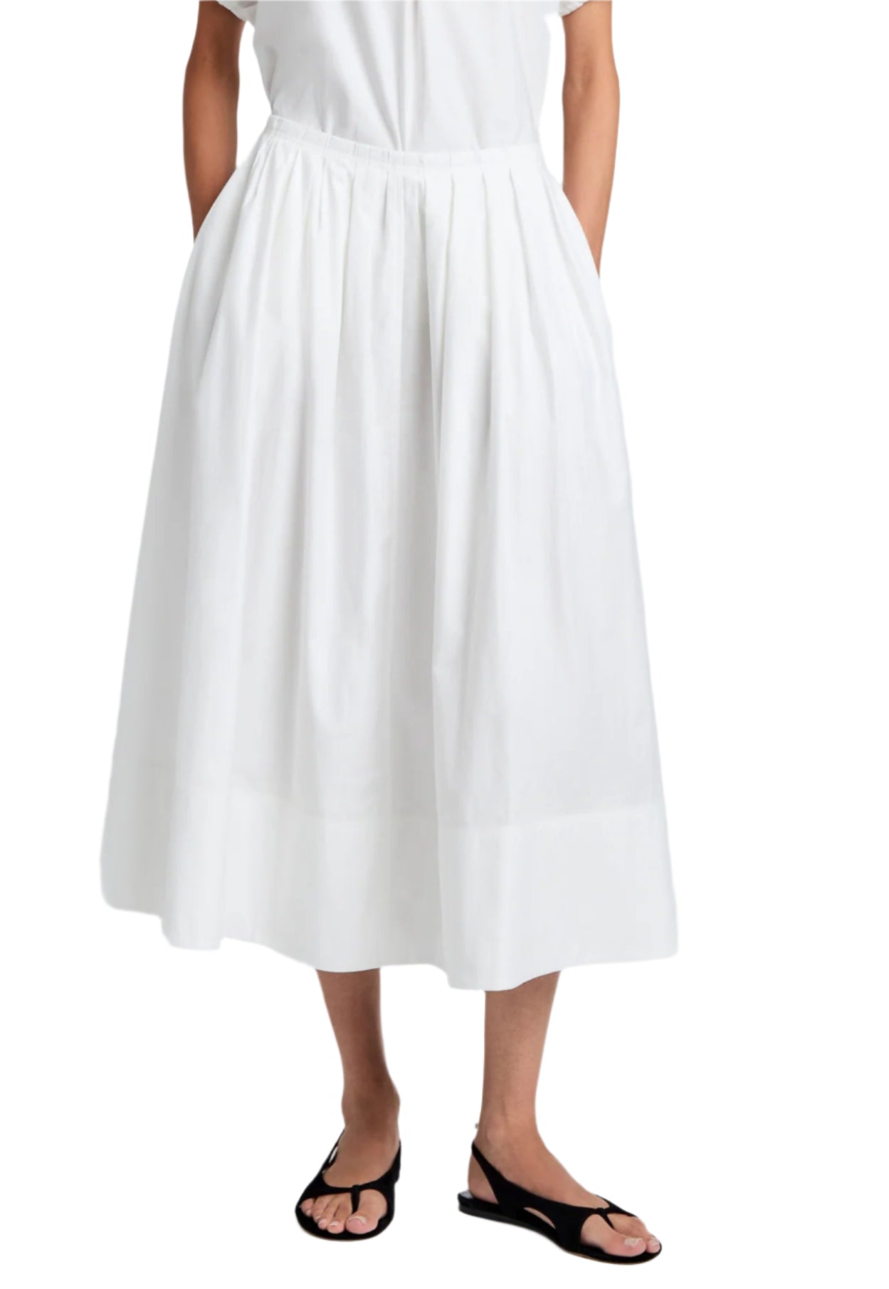 A person wearing the Proenza Schouler White Label Austin Skirt in white cotton sateen, knife-pleated and high-waisted, with hands in pockets, paired with black sandals.
