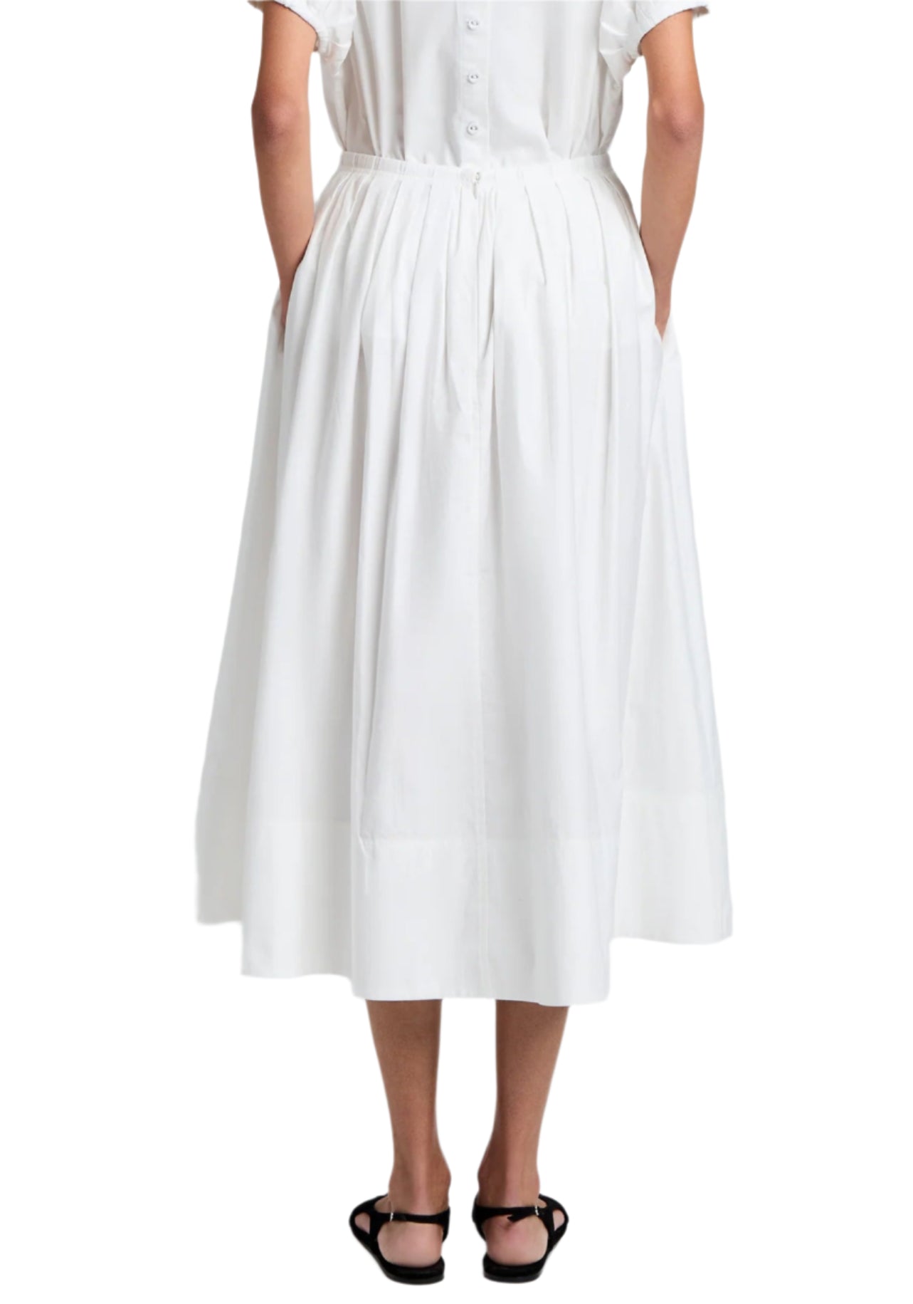 A person in a Proenza Schouler White Label Austin Skirt made of cotton sateen stands facing away, hands in pockets, while wearing black sandals.