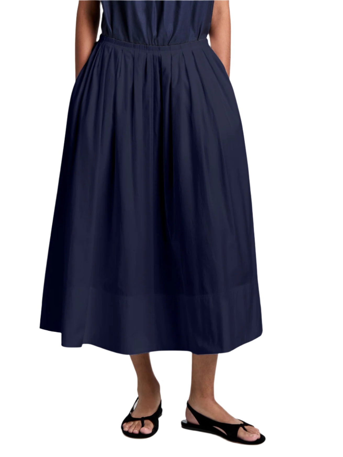 A person stands against a white background, hands in pockets, wearing the Proenza Schouler White Label Austin Skirt in navy cotton sateen with a subtle A-line silhouette and black sandals.