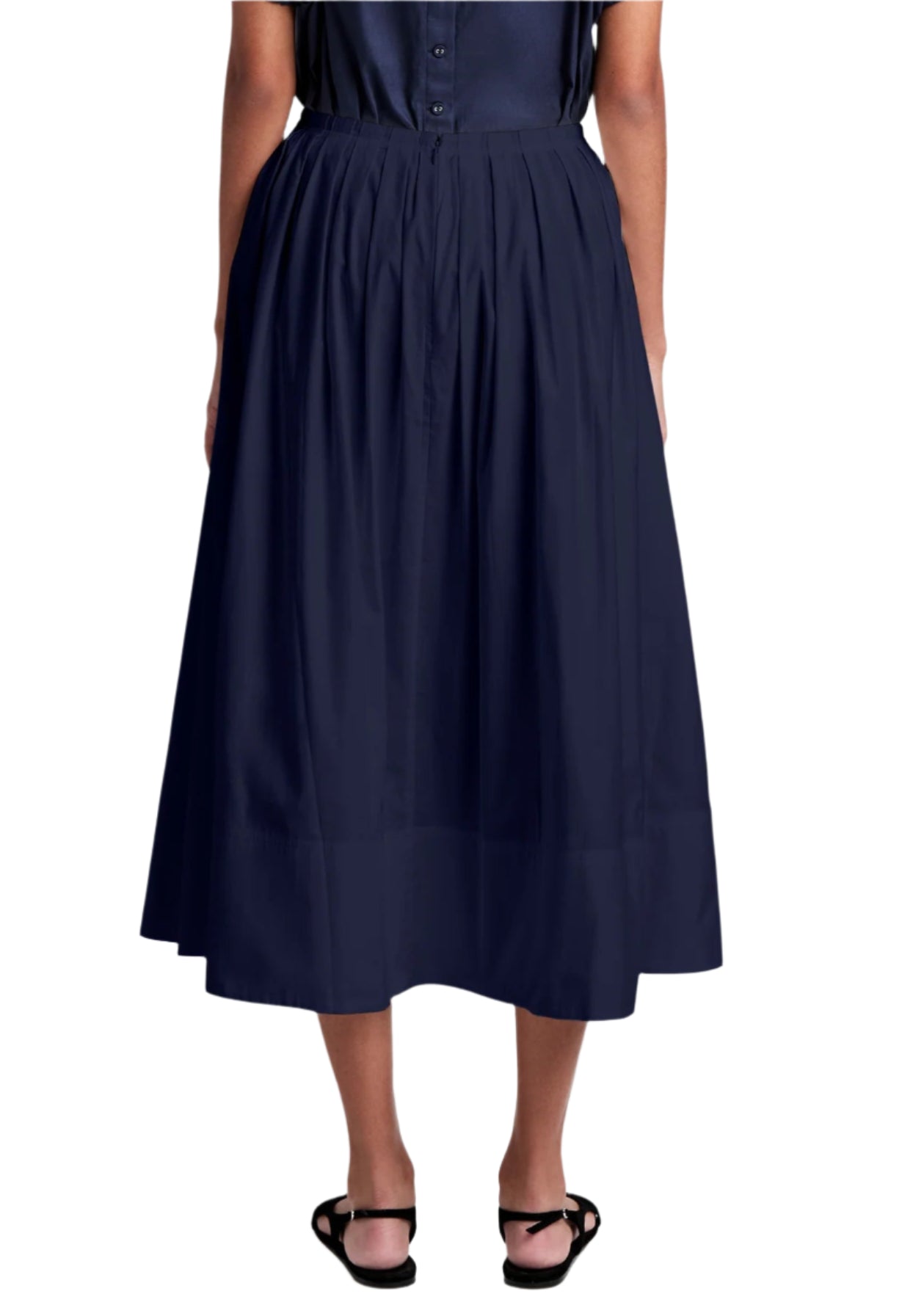A person is seen from the back, wearing a Proenza Schouler White Label Austin Skirt in navy blue cotton sateen with a graceful A-line silhouette, paired with black sandals.