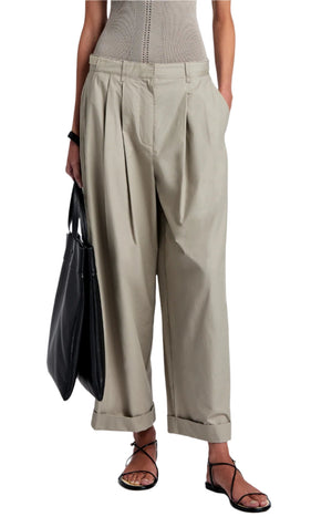The person is wearing wide beige trousers from the Proenza Schouler White Label Kyle Pant Brushed Poplin, along with a sleeveless top and holding a black bag, completed by black strappy sandals.