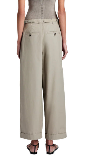 Rear view of a person wearing a beige top and Proenza Schouler White Label's Kyle Pant Brushed Poplin, highlighting the slouchy wide-leg design with cuffed hems, paired with black sandals.