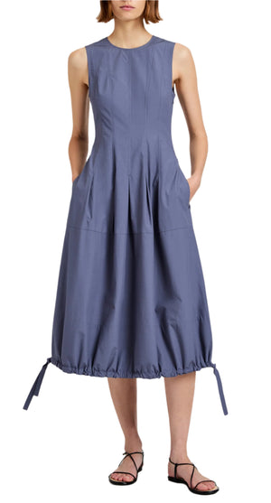A woman wears the Marley Brushed Poplin Dress by Proenza Schouler White Label, a sleeveless blue midi with an A-line silhouette, fitted bodice, flared skirt, drawstring hem, side pockets, and black strappy sandals.