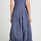 A woman stands with her back to the camera, wearing the Marley Brushed Poplin Dress by Proenza Schouler White Label—a sleeveless blue A-line midi with black buttons, pleats, and a gathered bubble hem with ties.
