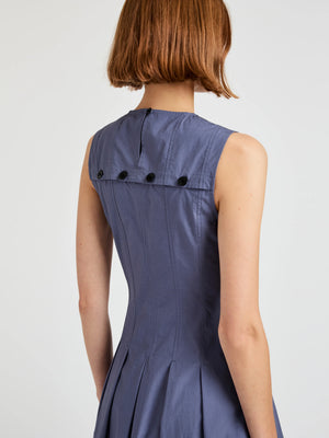 A person with short brown hair is seen from the back wearing the Marley Brushed Poplin Dress by Proenza Schouler White Label, a sleeveless, fitted blue dress with black buttons along the upper back and a subtle A-line shape.