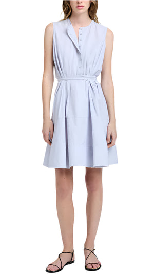 A woman wears the Kenzie Dress Linen by Proenza Schouler White Label, a sleeveless, light blue, knee-length fit-and-flare in Linen Shirting with buttons, waist tie, and black strappy sandals.