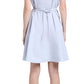 A woman with her back to the camera wears a sleeveless light blue Kenzie Dress Linen by Proenza Schouler White Label, featuring a waist tie and black sandals, highlighting its elegant fit-and-flare silhouette.