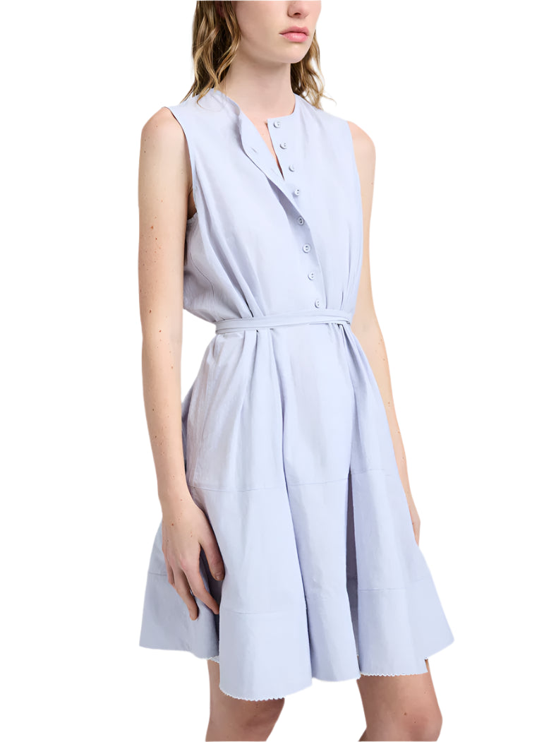 A woman stands against a plain background wearing the Proenza Schouler White Label Kenzie Dress Linen, a sleeveless light blue button-front dress with a belted waist and fit-and-flare silhouette.