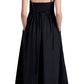 A person faces away, wearing the Proenza Schouler White Label Barker Dress Stretch Poplin in black with slim shoulder straps, layered over cream pants.