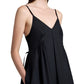 A woman wears the Proenza Schouler White Label Barker Dress Stretch Poplin, a sleeveless black A-line dress with slim shoulder straps and side pockets, shown from mid-chest to thigh.