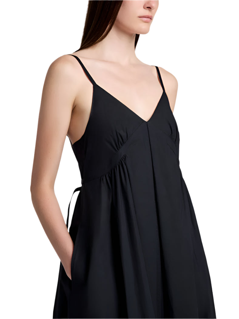 A woman wears the Proenza Schouler White Label Barker Dress Stretch Poplin, a sleeveless black A-line dress with slim shoulder straps and side pockets, shown from mid-chest to thigh.