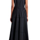 A woman faces away, wearing the Proenza Schouler White Label Kailey Dress Stretch Poplin— a sleeveless black pleated dress—paired with black flat sandals.