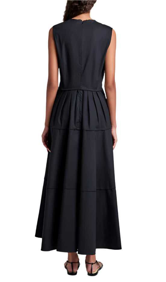 A woman faces away, wearing the Proenza Schouler White Label Kailey Dress Stretch Poplin— a sleeveless black pleated dress—paired with black flat sandals.