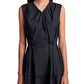 A woman wearing the Proenza Schouler White Label Kailey Dress Stretch Poplin, a sleeveless black fit-and-flare style with pleated neckline and waist, stands against a white background.